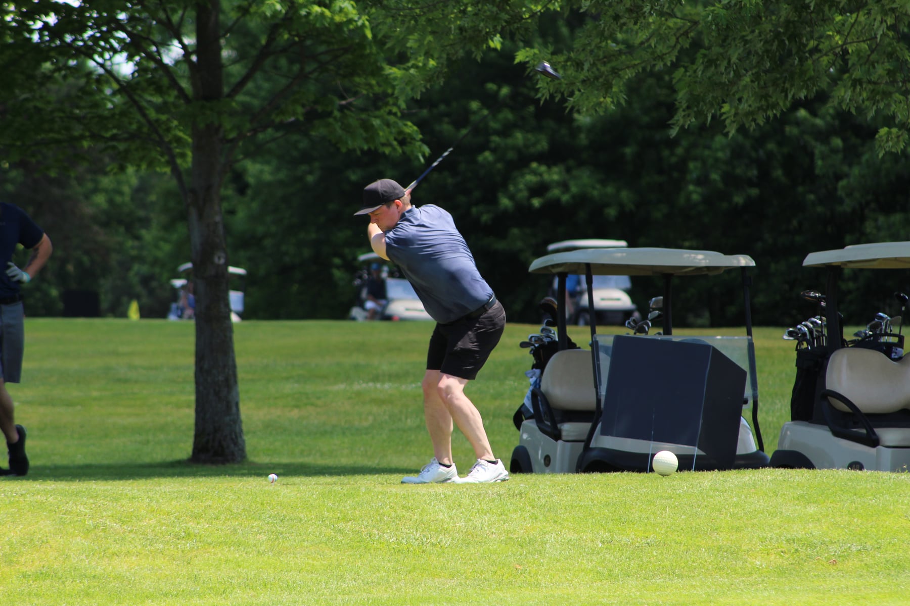 Golfers teeing off with carts nearby